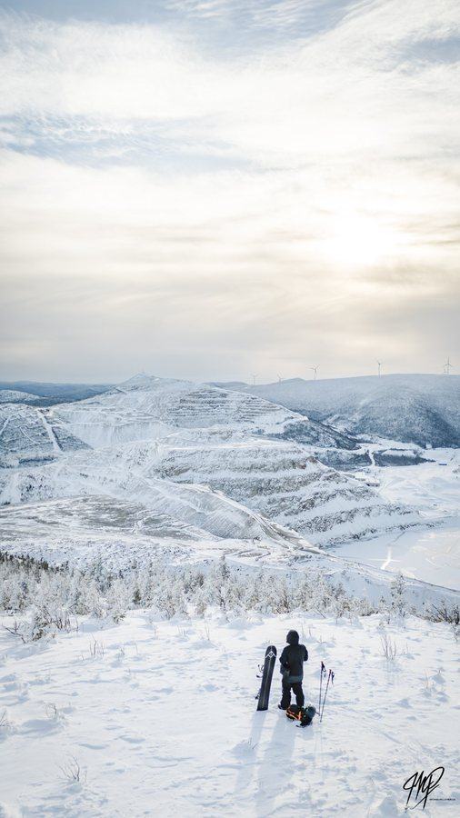 Splitboarder overlooking a snowy valley and wind turbines